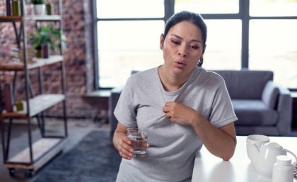 Woman leaning on bench holding glass of water looking hot and distressed. Adobe.